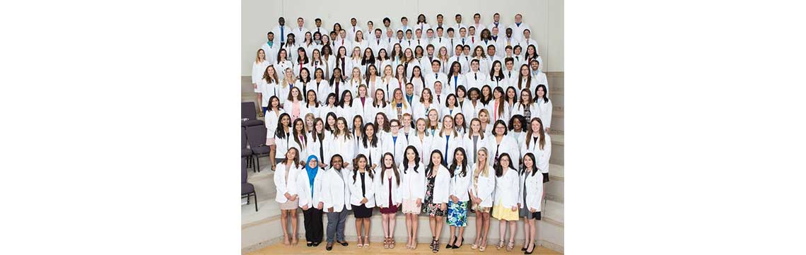 Large group of Pharmacy students wearing white coats standing on the steps of a lecture hall