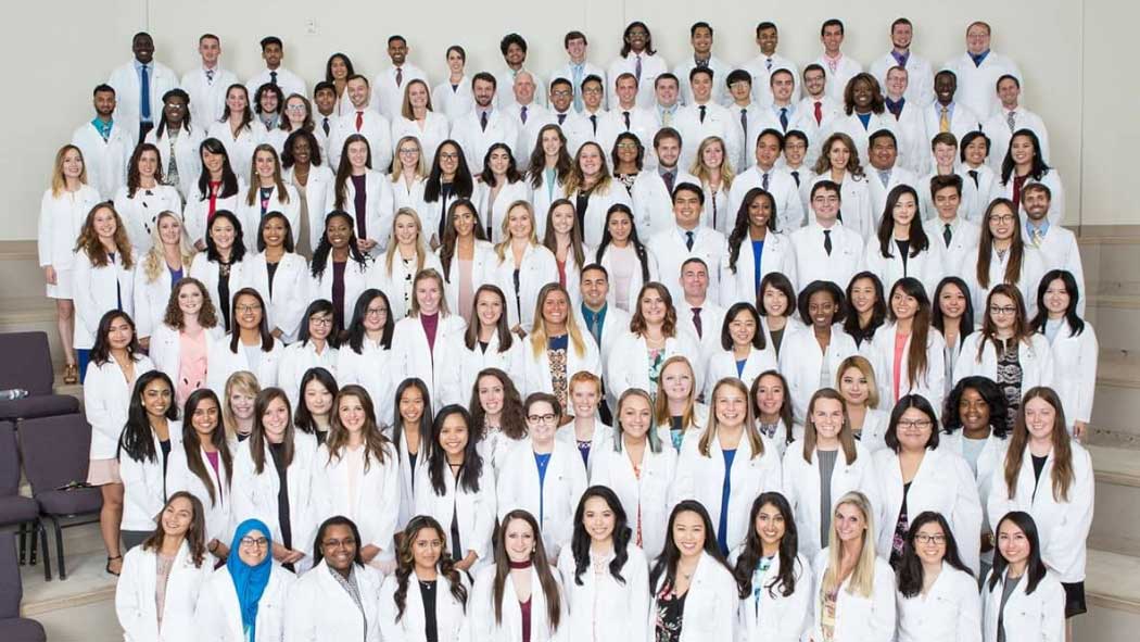 Large group of Pharmacy students wearing white coats standing on the steps of a lecture hall