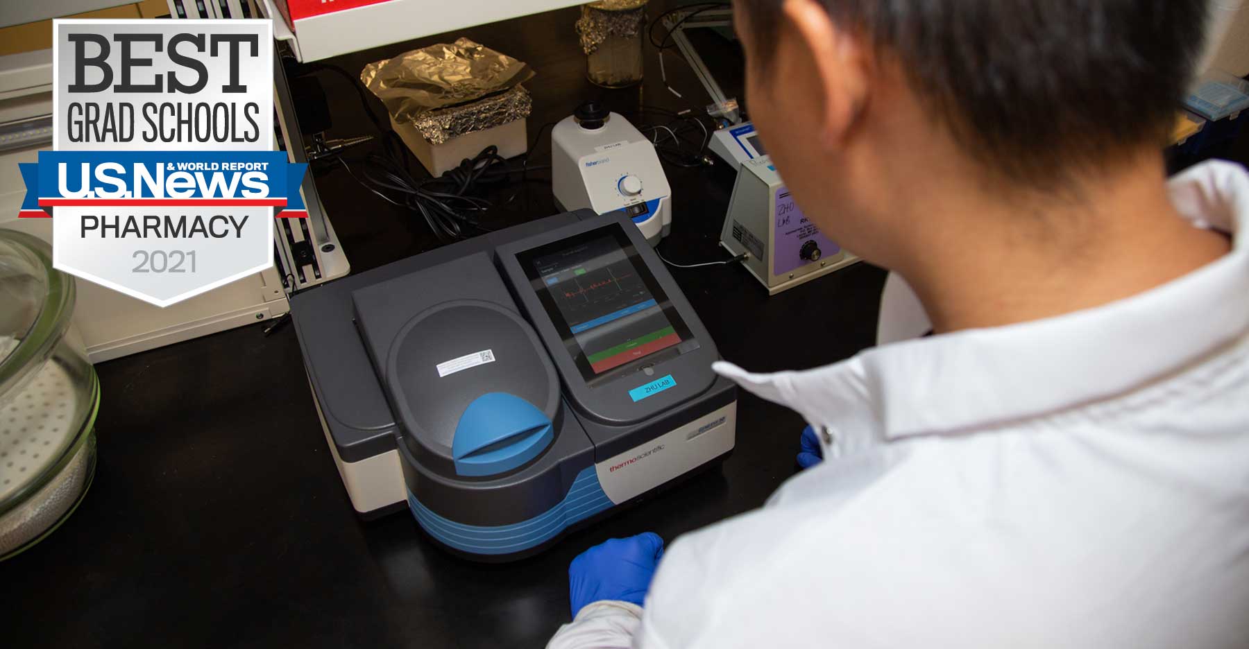 a pharmacy student using a piece of lab equipment alongside a u.s. news and world reports banner ranking v.c.u. school of pharmacy as a best grad school for 2021