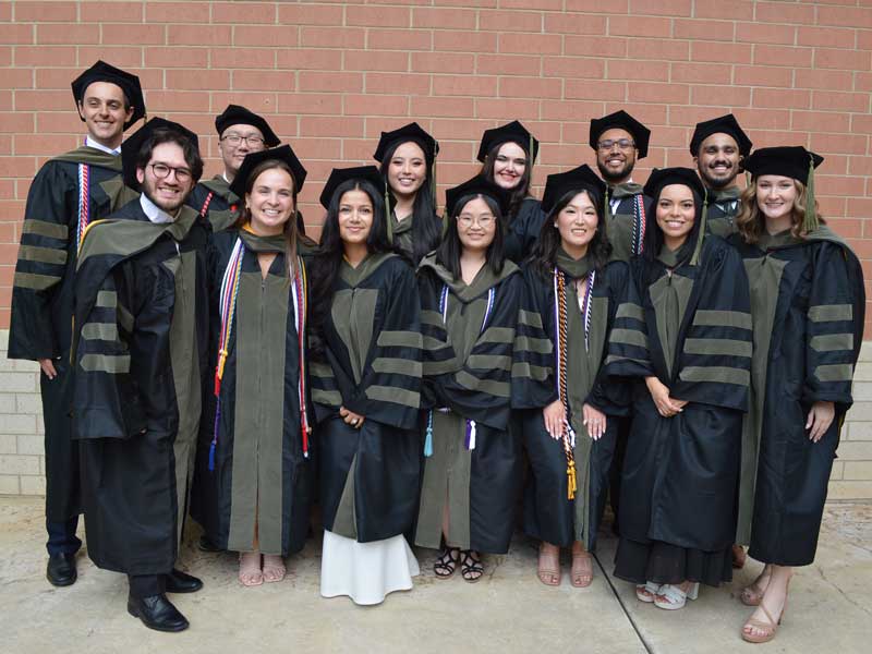 13 smiling people dressed in graduation ceremony caps and gowns