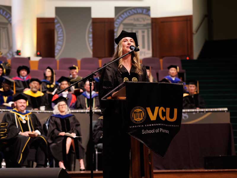 Ally Thompson in graduation regalia addresses the audience at the VCU School of Pharmacy Class of 2026 Hooding & Diploma Ceremony.