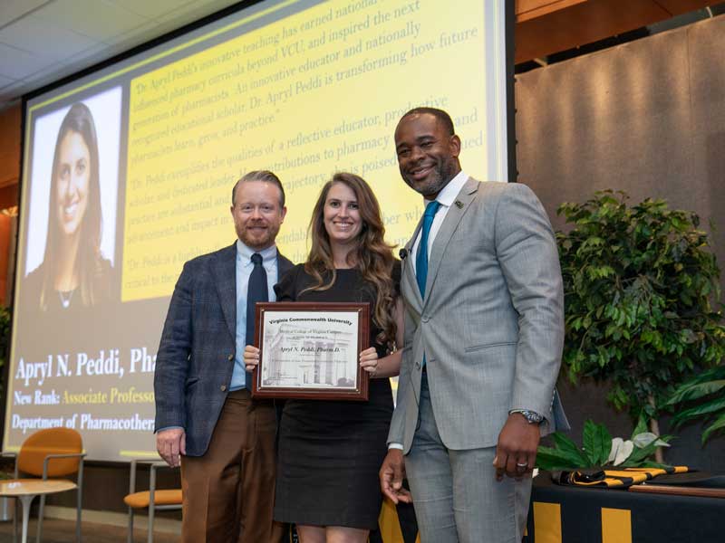 Standing between chair Dave Dixon and Dean K.C. Ogbonna, Apryl Peddi, Pharm.D., holds a plaque following her promotion