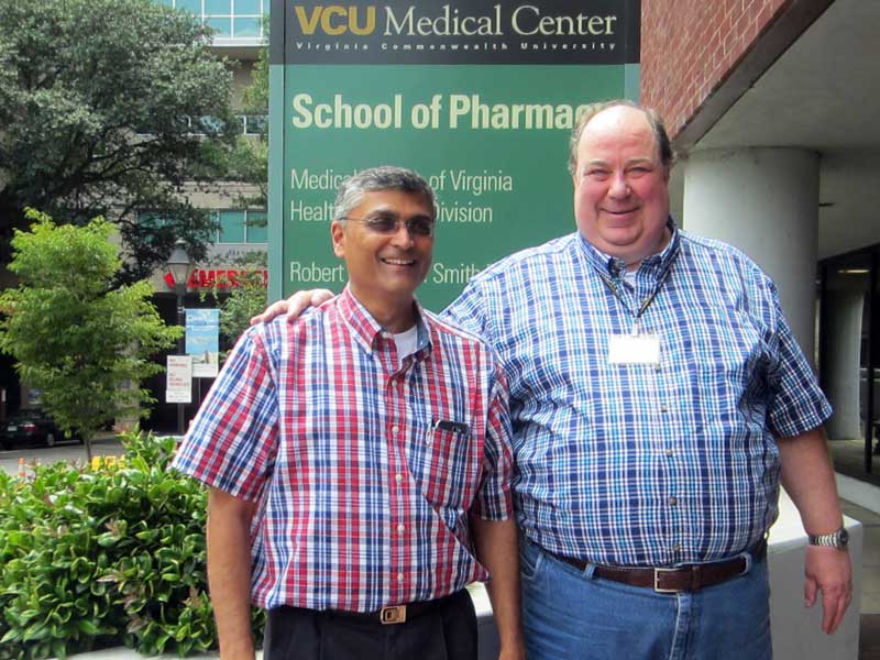 Dr. Umesh Desai, chair of the Department of Medicinal Chemistry, and Dr. Jurgen Venitz, longtime professor of pharmaceutics, smile together for a photo in front of a sign in front of the VCU School of Pharmacy's Smith Building
