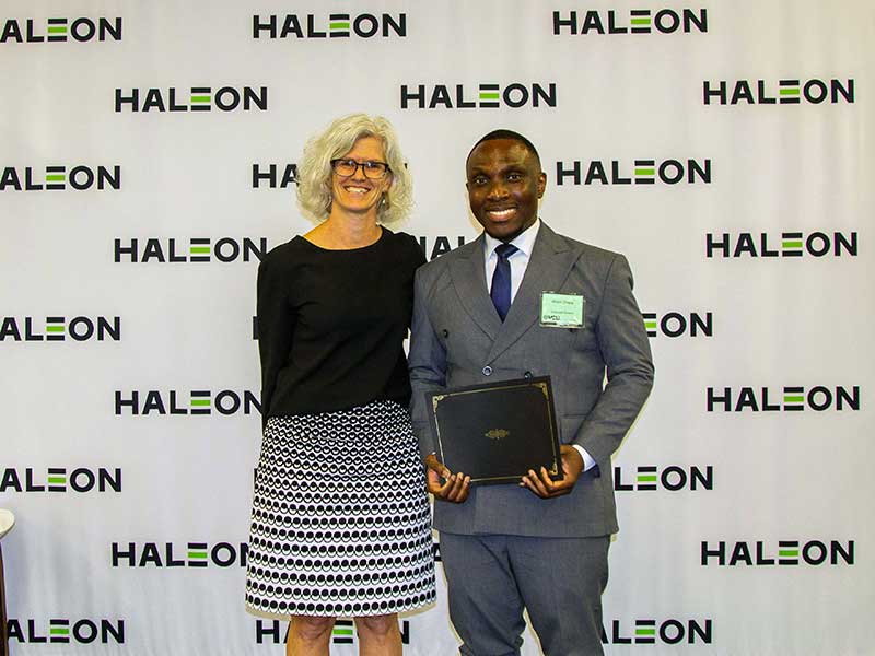 A student holding an award stands next to the associate dean for research and graduate studies in front of a backdrop that has the Haleon logo