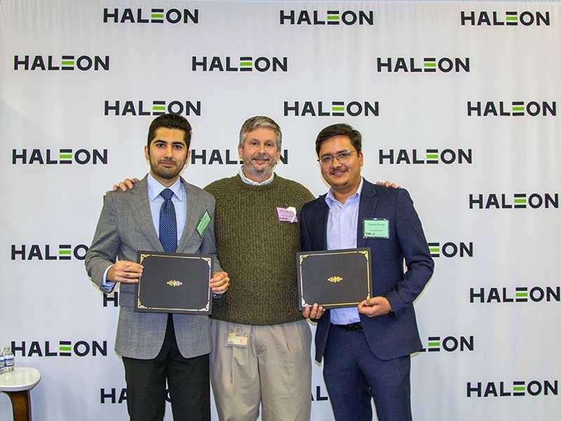 Students holding awards stand next to the department chair of Pharmaceutics in front of a backdrop that has the Haleon logo