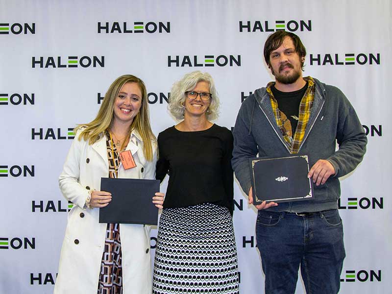 Students holding awards stand next to the associate dean for research and graduate studies in front of a backdrop that has the Haleon logo