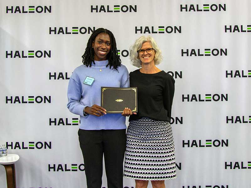 A student holding an award stands next to the associate dean for research and graduate studies in front of a backdrop that has the Haleon logo