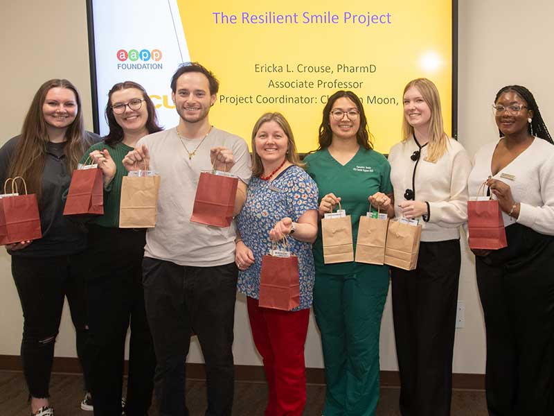 A group photo of six students and one faculty member holding small paper bags full of dental hygiene supplies with handles.