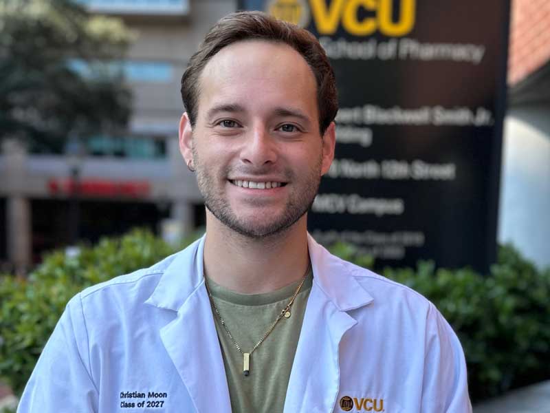 Christian Moon, wearing a VCU School of Pharmacy white coat with his name and 