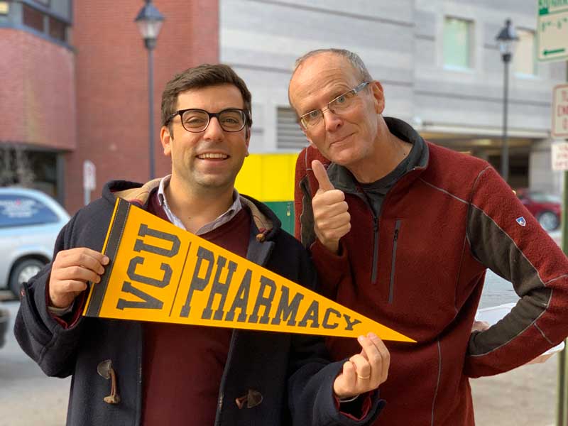 Dr. Holdford and Dr. Pontinha smile together for a photo while Dr. Pontinha holds a VCU Pharmacy pennant just before Dr. Pontinha graduates from VCU School of Pharmacy in 2022.