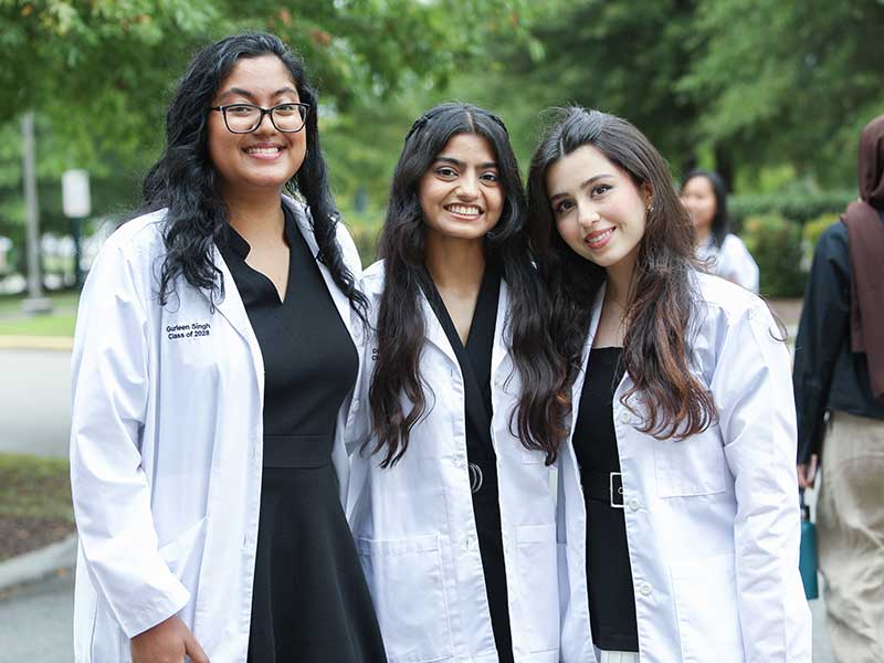 Three students smile while wearing v c u pharmacy white coats.