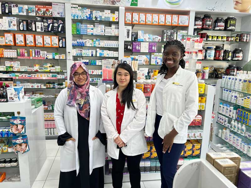 two v.c.u. pharmacy students standing with a pharmacist in a pharmacy