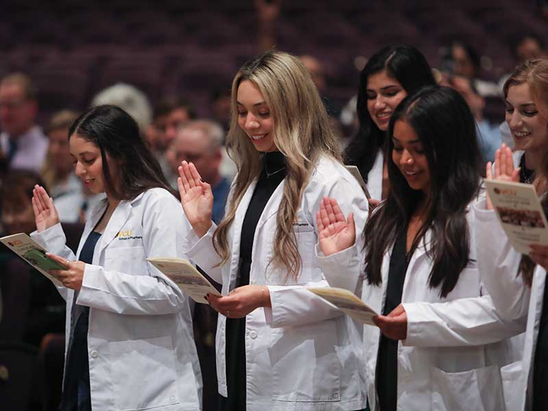 Three students raise hands while taking pharmacy oath.