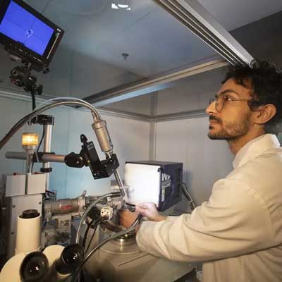 a lab worker in a pharmaceutical lab completes a task using a piece of lab equipment while monitoring his work on a nearby t.v. screen