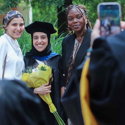 a graduate dressed in regalia posing with friends at a commencement ceremony