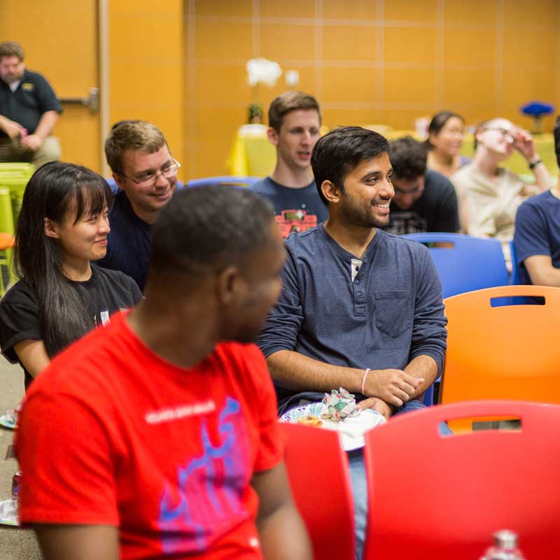 Group of students sitting in small classroom auditorium chairs laughing.