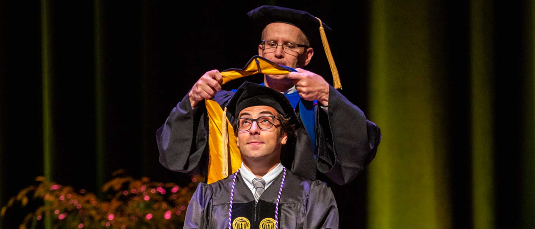 a professor places doctoral hood on student at graduation ceremony.