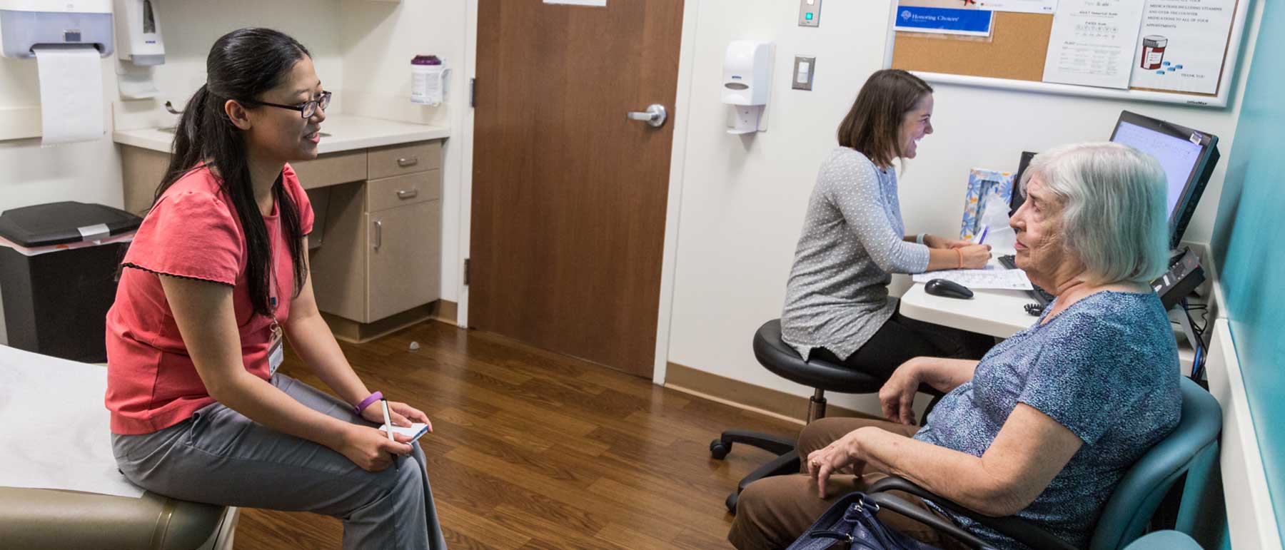 A pharmacist and student talk with a patient in a clinic.