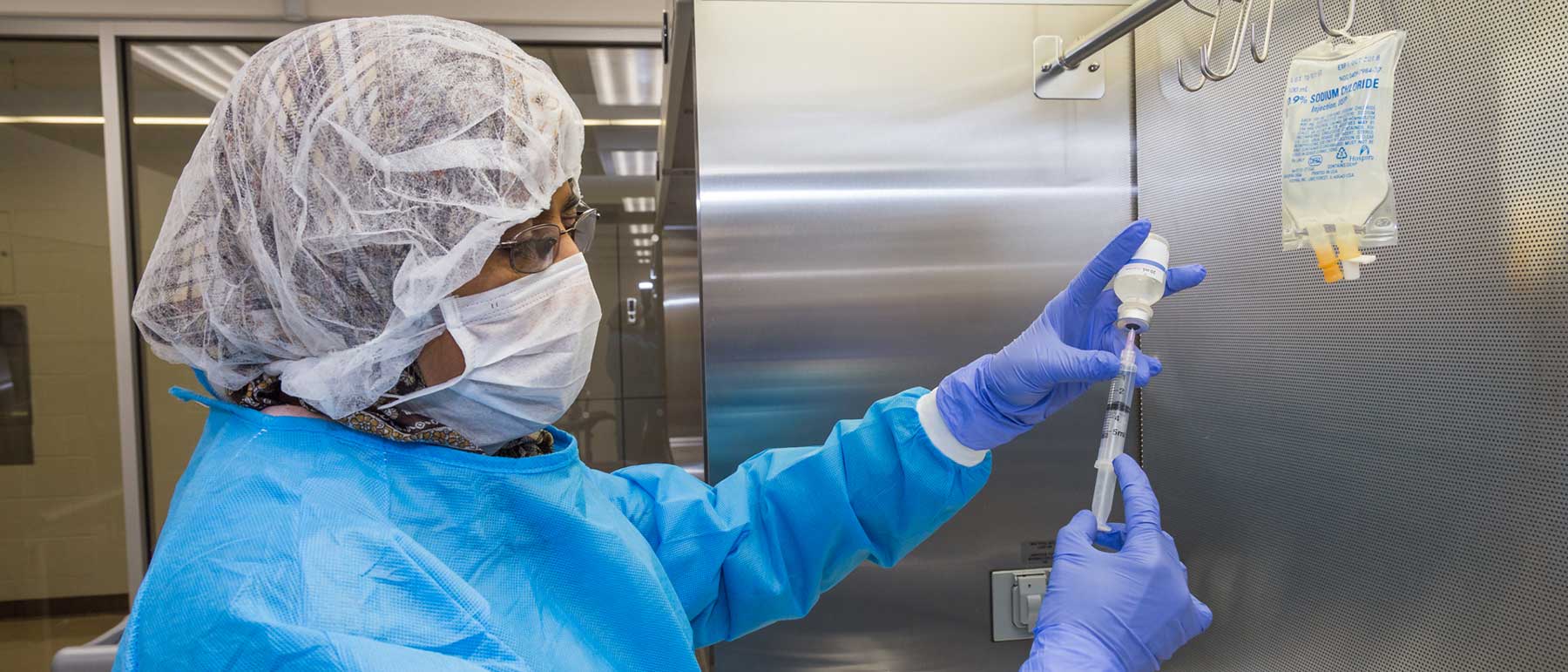 A researcher wearing sterile clothing fills a syringe.