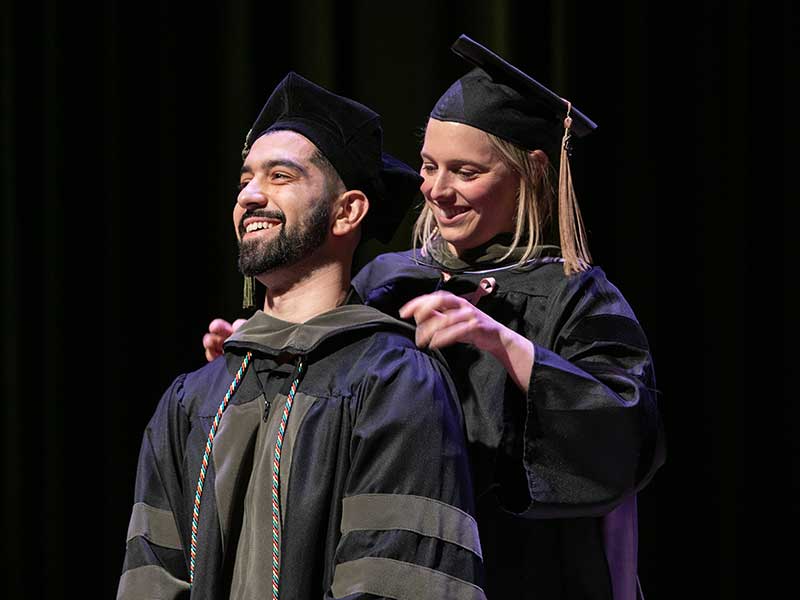 A professor places a graduation hood on a student.