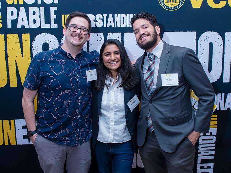 Three students stand in front of v c u branded backdrop.