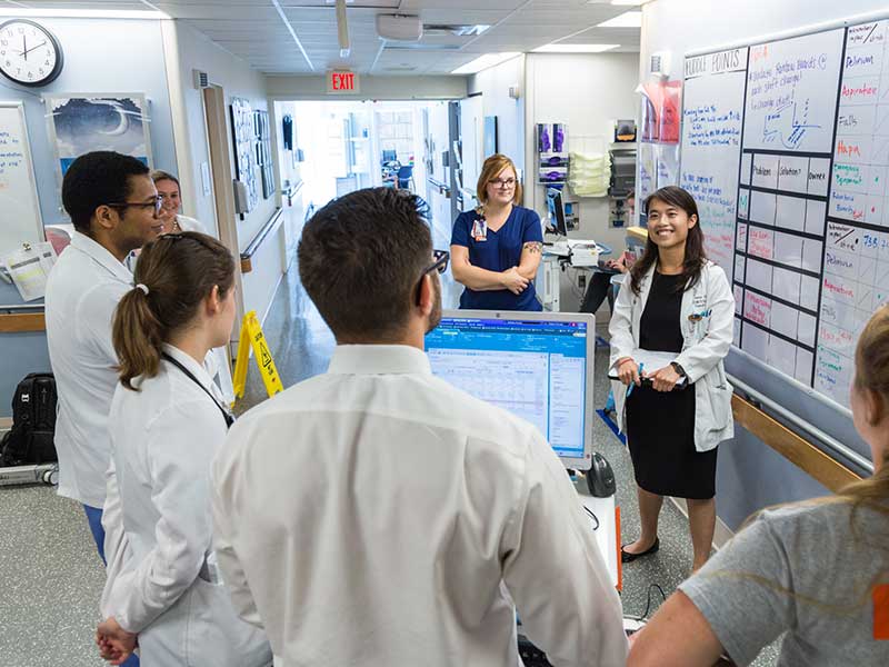 A group of students stand in a hospital hallway looking a chart.