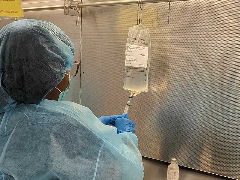 a lab worker in sterile dress extracts liquid from an i.v. in a lab using a syringe