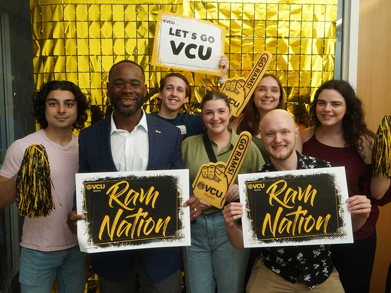 v c u dean Ogbonna poses with students holding v c u pharmacy signs.