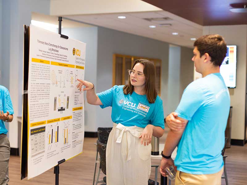 A student explains a research poster to another student.