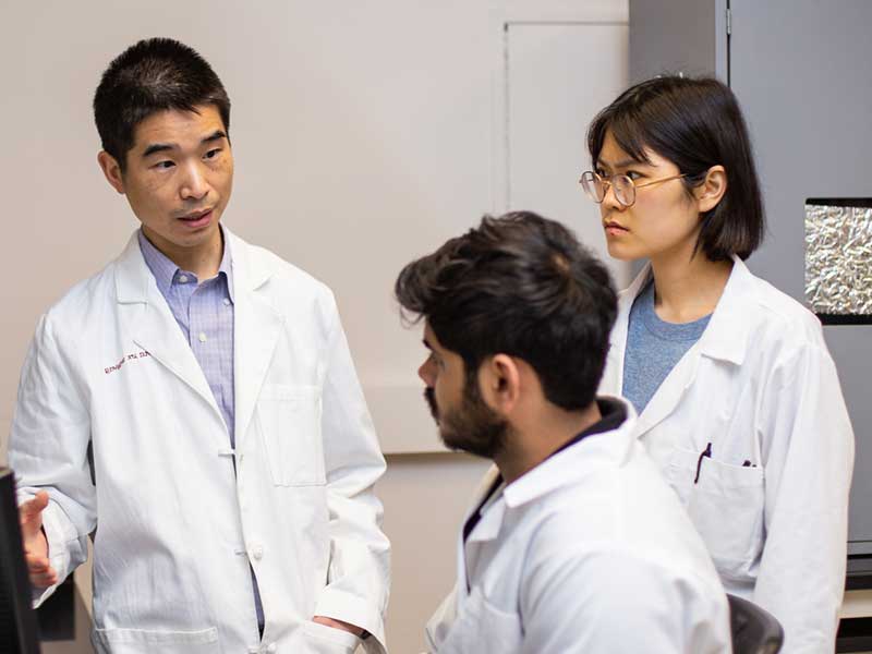 A professor talking to two students in a research lab.