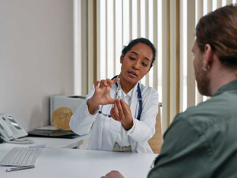 a pharmacist holds up a syringe full of medicine and counsels a patient