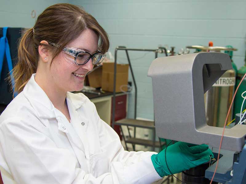 a lab worker smiles while doing work on a machine in a pharmaceutics lab