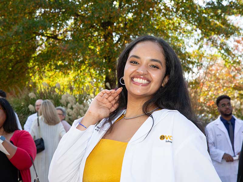 A student wears a v c u pharmacy white coat smiling.