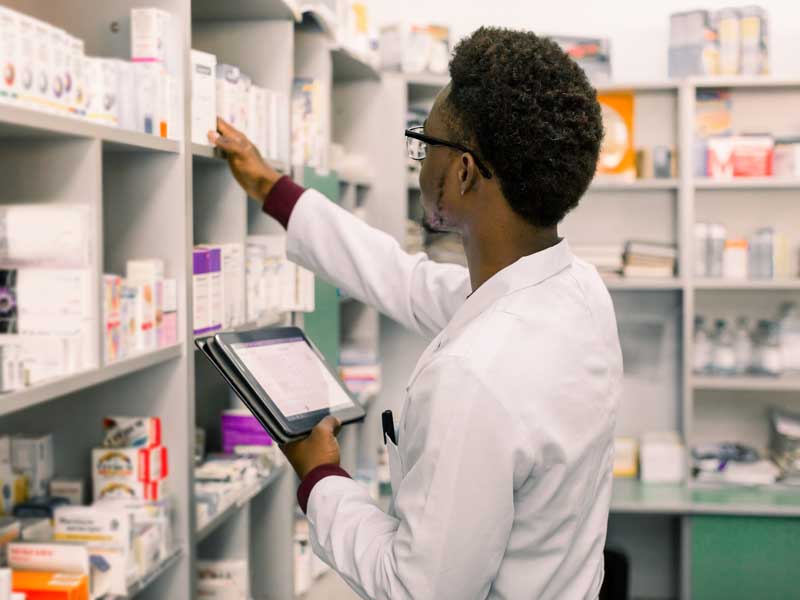 a pharmacy worker takes inventory of medications on a pharmacy shelf