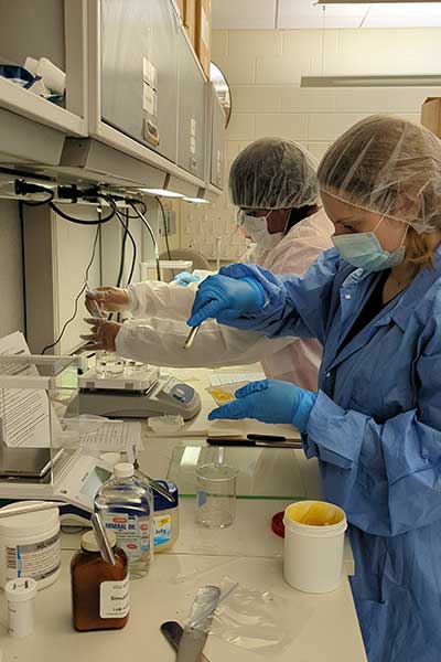 Two students in full personal protective equipment work in the lab measuring materials.