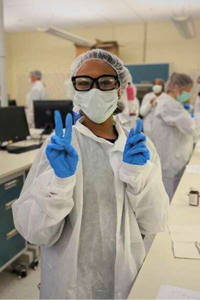 A student in full personal protective equipment stands and smiles in lab.