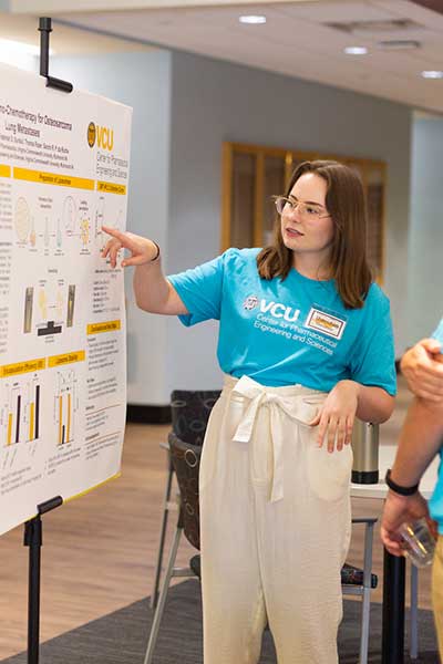 A student points to details of her poster presentation to an onlooking guest