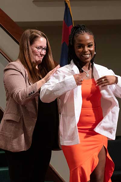 A pharmacy professor places white coat on student