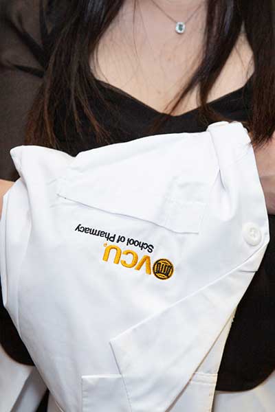 White coat with VCU School of Pharmacy logo folded over a womens arm.