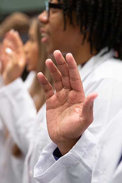 Students in white coats raise their right hand to recite oath.